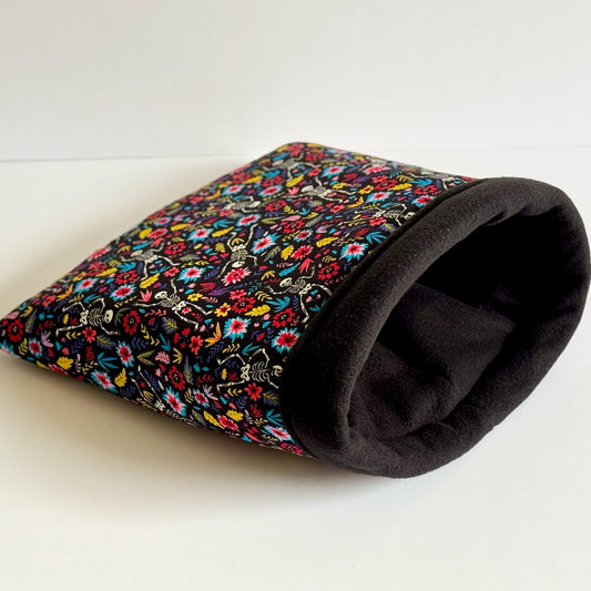 The Blooms & Bones Snuggle Sack enchants with a gothic-glam twist—its plush black fleece interior invites your guinea pig into cozy shadows, while the outside bursts with vibrant florals entwined with playful bone motifs. Pictured on a moonlit-white background, this snug hideaway is perfect for your little familiar who dreams of midnight gardens and charmingly spooky naps.