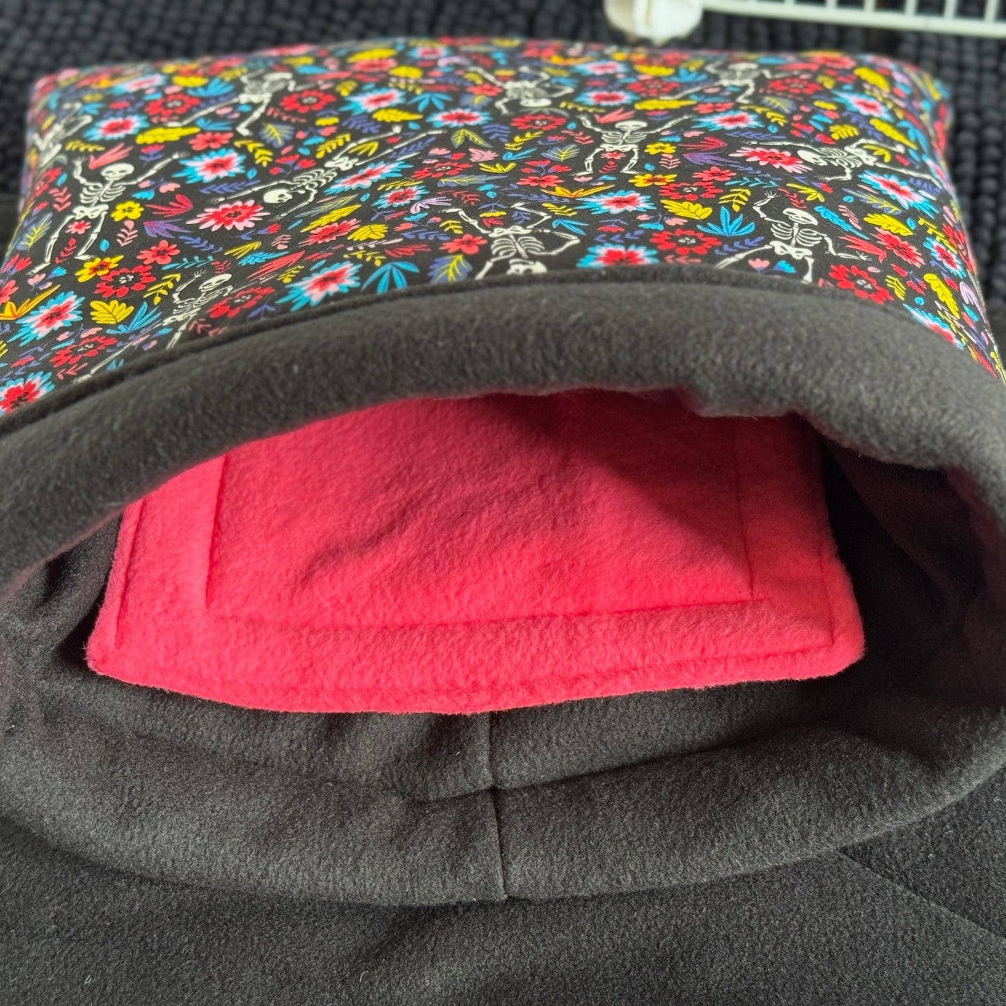 The Blooms & Bones Snuggle Sack enchants with a gothic-glam floral crown atop a midnight black exterior, cradling your guinea pig or little familiar in plush pink fleece. Perfectly spooky-cute, this snuggly haven cocoons your small pet in cozy magic—and looks hauntingly lovely resting on any shadowy, textured lair.