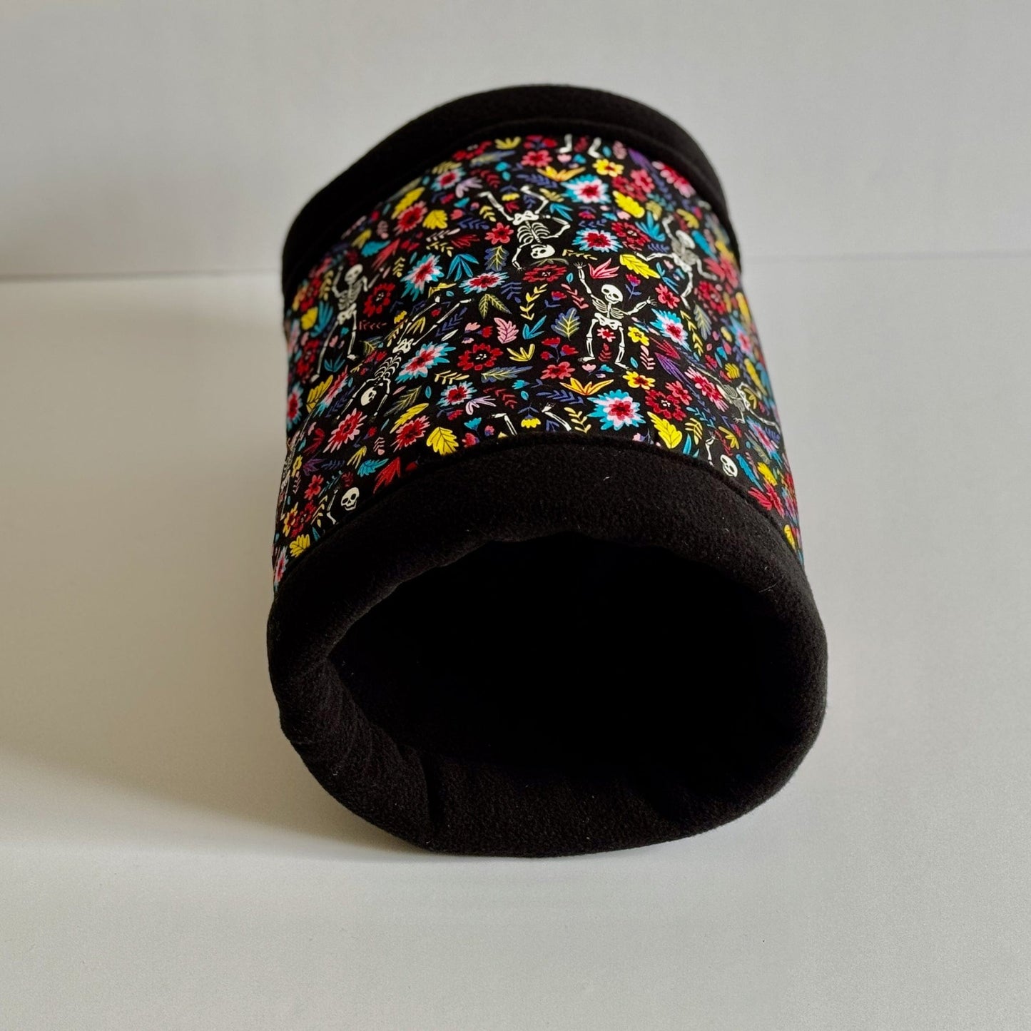 The Blooms & Bones Fleece Tunnel is a cozy gothic-glam hideaway for small pets—a plush black tunnel adorned with vibrant, enchanting florals twined around cheerful little skeletons. This hauntingly sweet print from the Blooms & Bones collection adds a spellbinding pop of color and whimsy. Displayed on a crisp white background, it’s the purrfect blend of spooky-cute style for guinea pigs and other tiny creatures who adore a dash of dark elegance in their lair.