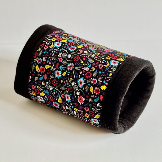 The Blooms & Bones Fleece Tunnel conjures gothic glamour with its cozy, jet-black fleece lining and a spellbinding print of vibrant flowers entwined with playful candy-colored skeletons. Perfectly cylindrical for scurrying or snuggling, this tunnel invites your small pet to embrace their inner creature of the night in comfort and style. Photographed against a plain white background for an enchanting pop of contrast.