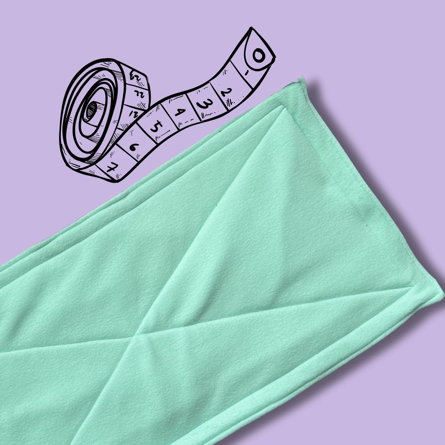 A bewitchingly soft, mint green fabric—folded with care—rests atop a rich, purple backdrop like a moonlit mist. Beside it, a black and white illustrated measuring tape curls enchantingly, its bold numbers peeking out in gothic style, ready to measure your beloved familiar for the perfect whimsical accessory.