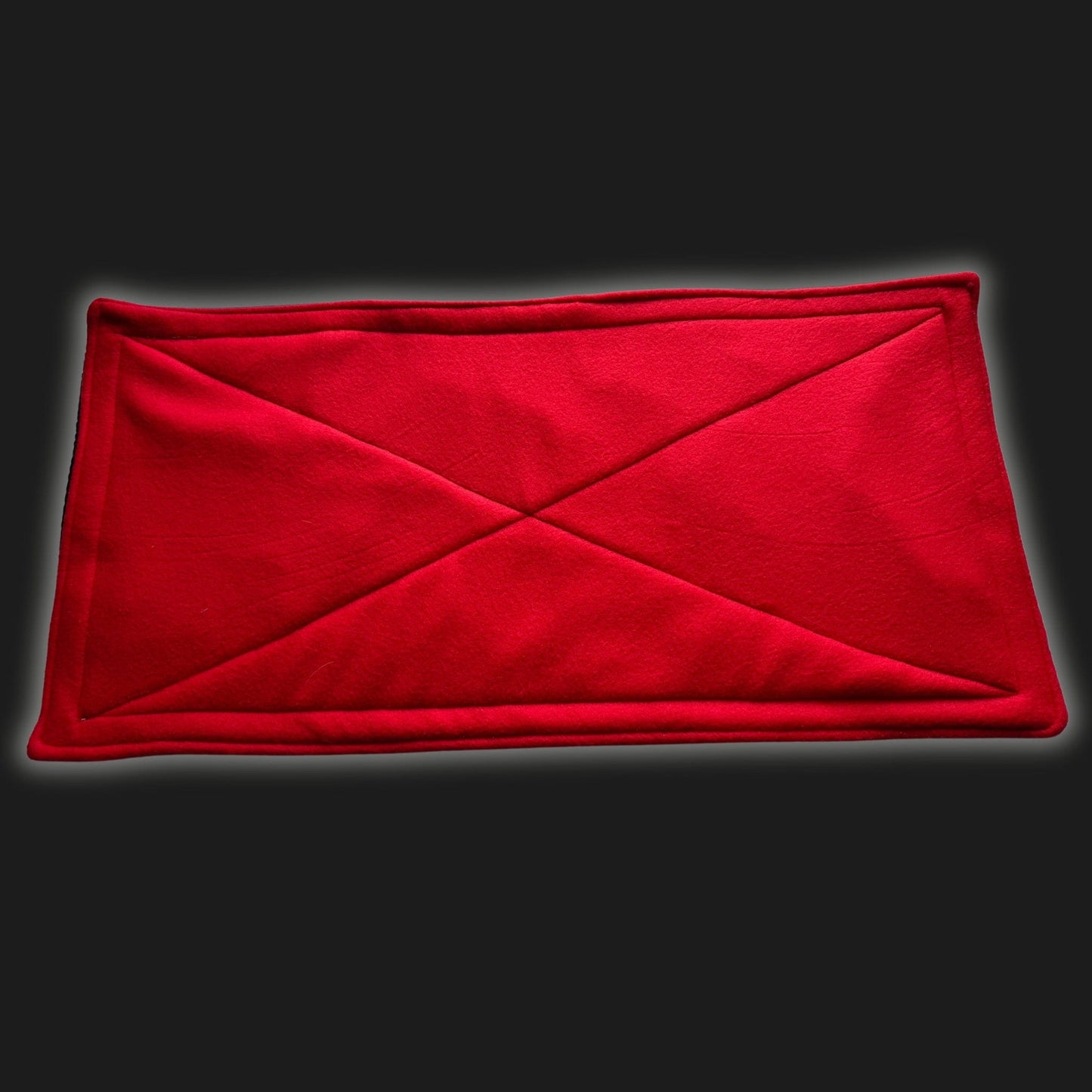 A bewitching red Modular Fleece Liner & Pee Pad, adorned with stitched diagonal X patterns like secret gothic runes, rests atop a shadowy black backdrop. This cozy, waterproof pad is perfect for pampered guinea pigs and little familiars—magically whisking away mess to keep their enchanted lair snug and dry.