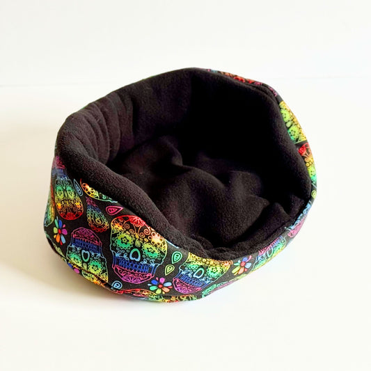 Enchanted in midnight fleece, this pet bed flaunts a lively sugar skull rim and bright blooms—a gothic-cute snuggle haven for guinea pigs.