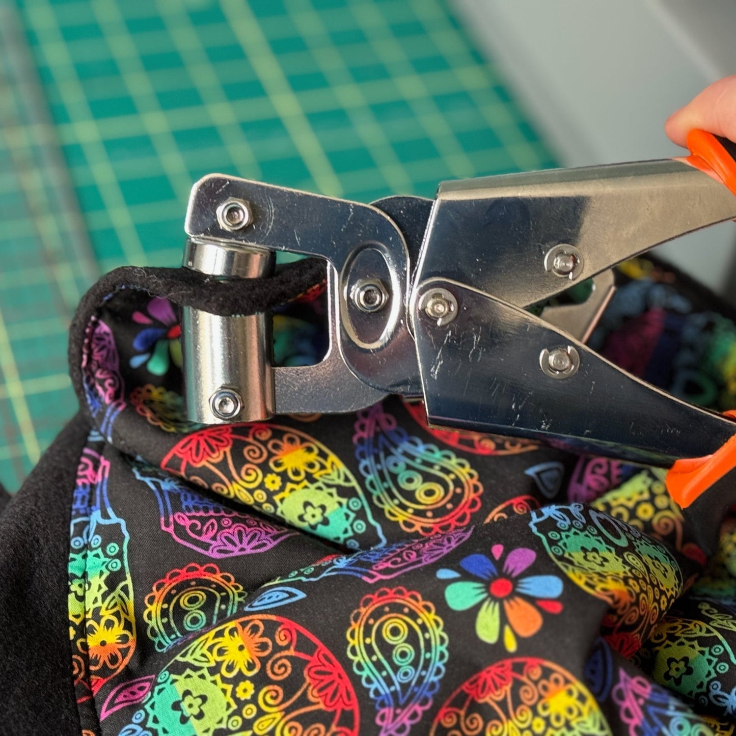 In a bewitchingly creative workspace, nimble hands wield a tool to press a grommet into swirling paisley fabric—rich with inky blacks and vibrant scarlets—to conjure the Frightful Fiesta Corner Fleece Forest. This gothic-glam hideaway, perfect for guinea pigs seeking midnight adventures or cozy naps in their C&C castle, awaits atop a moss-green cutting mat sprinkled with trimmings and hints of spooky-chic magic.