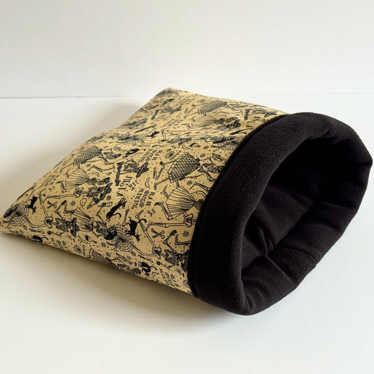 The Tombstone Tango Snuggle Sack is a bewitchingly cozy tunnel for guinea pigs, draped in tan and midnight-black hues. Its exterior flaunts gothic vintage-style tombstones and swirling motifs, while the inside beckons with velvety soft black fleece—perfect for midnight naps or haunted hide-and-seek. Pictured resting on a snowy white backdrop, this snug lair invites your little companion to dance with dreams on the spooky-cute side.
