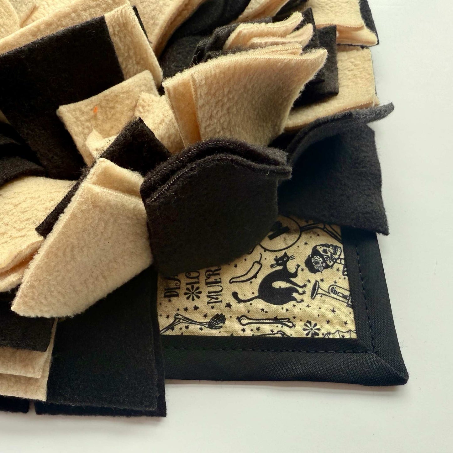 A close-up of the Tombstone Tango Snuffle Mat—cream and midnight fleece strips over spooky-cute black cat fabric, bordered in black.
