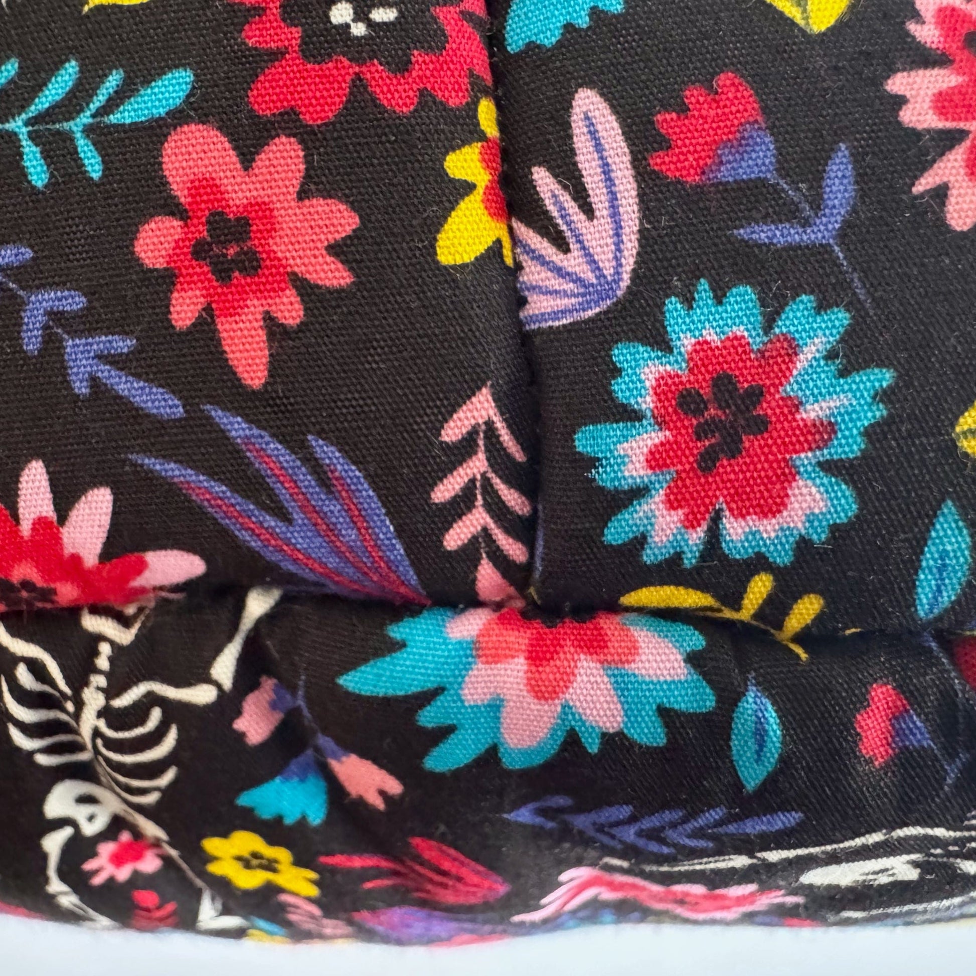 Spooky-cute close-up of our Blooms & Bones Fleece Bed fabric: dramatic black fleece adorned with enchanting bursts of magenta, violet, and crimson blooms, weaving through a mysterious partial white skeleton. Perfectly plush for pampered guinea pigs or other petite familiars seeking cozy gothic-glam slumber!.