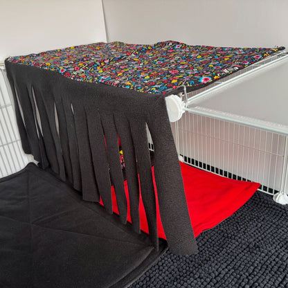 A cozy small animal cage transformed into a gothic-glam hideaway, with two tiers of wire shelves draped in vibrant, floral fleece and velvety black curtains. The whimsical Blooms & Bones Haybox Fleece Forest canopy casts playful shadows above plush red and midnight-black bedding. Below, a textured black mat completes this mysterious yet utterly adorable sanctuary—perfect for little ghouls like guinea pigs or other pocket-sized familiars seeking snuggly comfort.