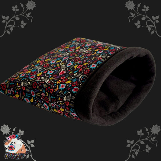 The Blooms & Bones Snuggle Sack is a plush black fleece tunnel, lovingly adorned with lush, gothic-inspired blooms in shades of crimson and violet. Delicate rose accents haunt the dark background, while a whimsically illustrated guinea pig—rosy-cheeked and beaming—peeks from the lower left corner like a tiny phantom of coziness. Perfectly sized for guinea pigs or other small creatures craving snuggly shelter in haunted-floral splendor.