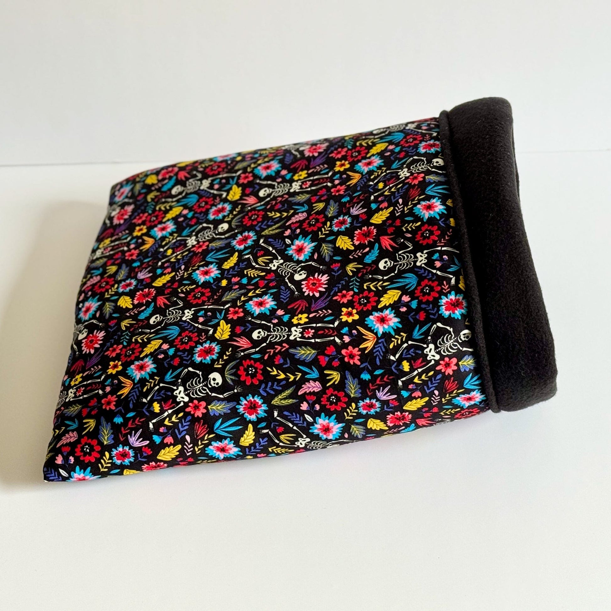 A cozy-chic haven for your littlest familiars, the Blooms & Bones Snuggle Sack enchants with plush, midnight-black fleece lining and an outer layer blossoming with vivid gothic florals—pops of crimson, violet, and emerald swirling upon an inky black backdrop. Perfectly sized for guinea pigs and other small companions seeking warmth on misty nights. Pictured folded neatly atop a ghostly white surface, ready to cradle your pet in dark elegance.