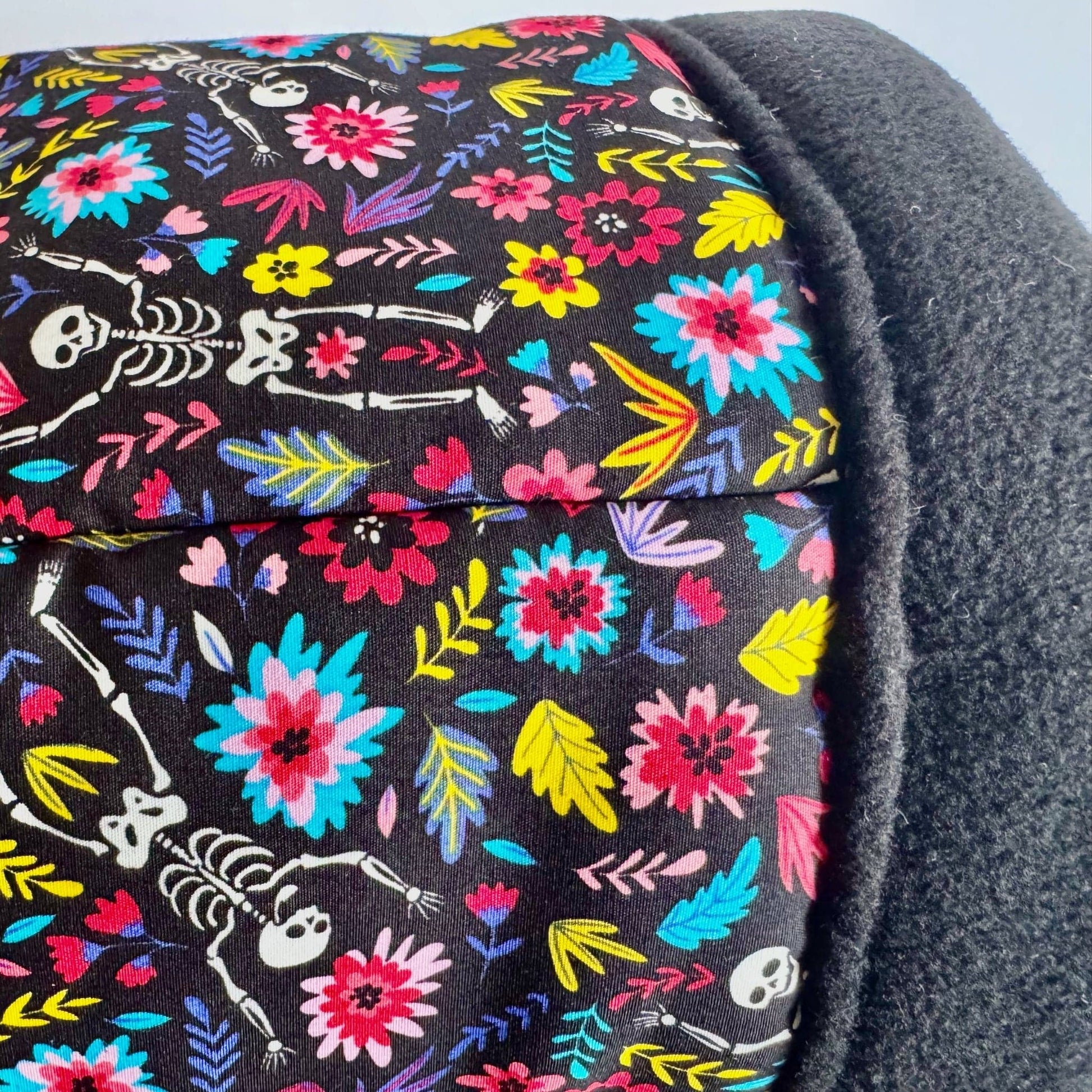 A close-up of luxuriously soft black fabric adorned with vivid, enchanted blossoms and playful white skeletons, all framed in velvety midnight-gray fleece—an irresistibly cozy retreat for small pets who crave a dash of gothic garden magic. Perfect for the Blooms & Bones Fleece Tunnel collection.