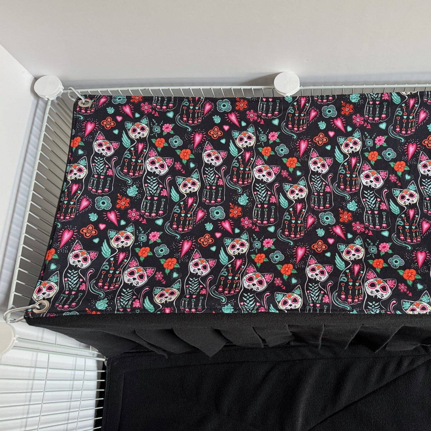 The Curious Catrina Haybox Fleece Forest is a delightfully eerie, soft rectangular fleece blanket adorned with enchanting sugar skull cats and vibrant gothic florals swirling across a midnight-black background. This cozy creation invites your small pet to burrow beneath charmingly spooky patterns, lending a dash of gothic-glam allure and snuggly comfort to any wire enclosure.