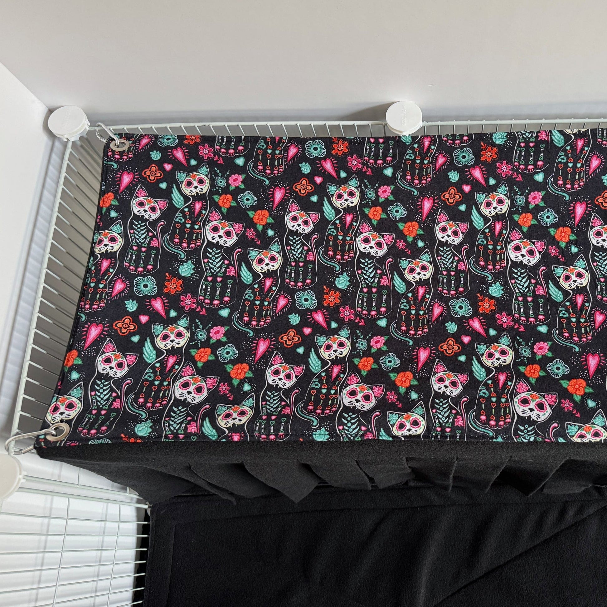The Curious Catrina Haybox Fleece Forest is a delightfully eerie, soft rectangular fleece blanket adorned with enchanting sugar skull cats and vibrant gothic florals swirling across a midnight-black background. This cozy creation invites your small pet to burrow beneath charmingly spooky patterns, lending a dash of gothic-glam allure and snuggly comfort to any wire enclosure.