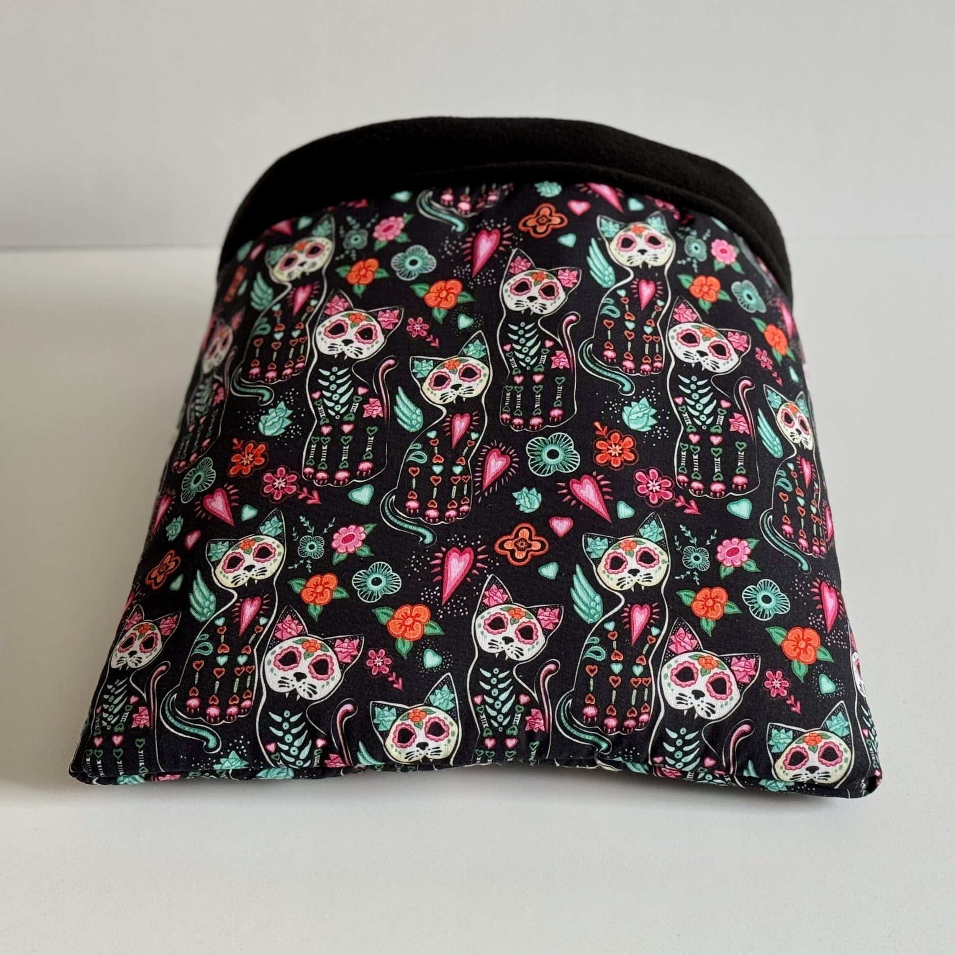 Enchant your little familiar with the Curious Catrina Snuggle Sack—an irresistibly cozy pouch crafted in gothic-glam style. Bewitching midnight-black fabric is adorned with whimsical Day of the Dead skeleton kitties, radiant flowers, and charming heart motifs in vivid candy colors. The plush black fleece lining invites guinea pigs or other small companions to burrow deep into mysterious comfort. Finished with a sleek black trim for extra drama—perfect for cuddles and midnight mischief!.