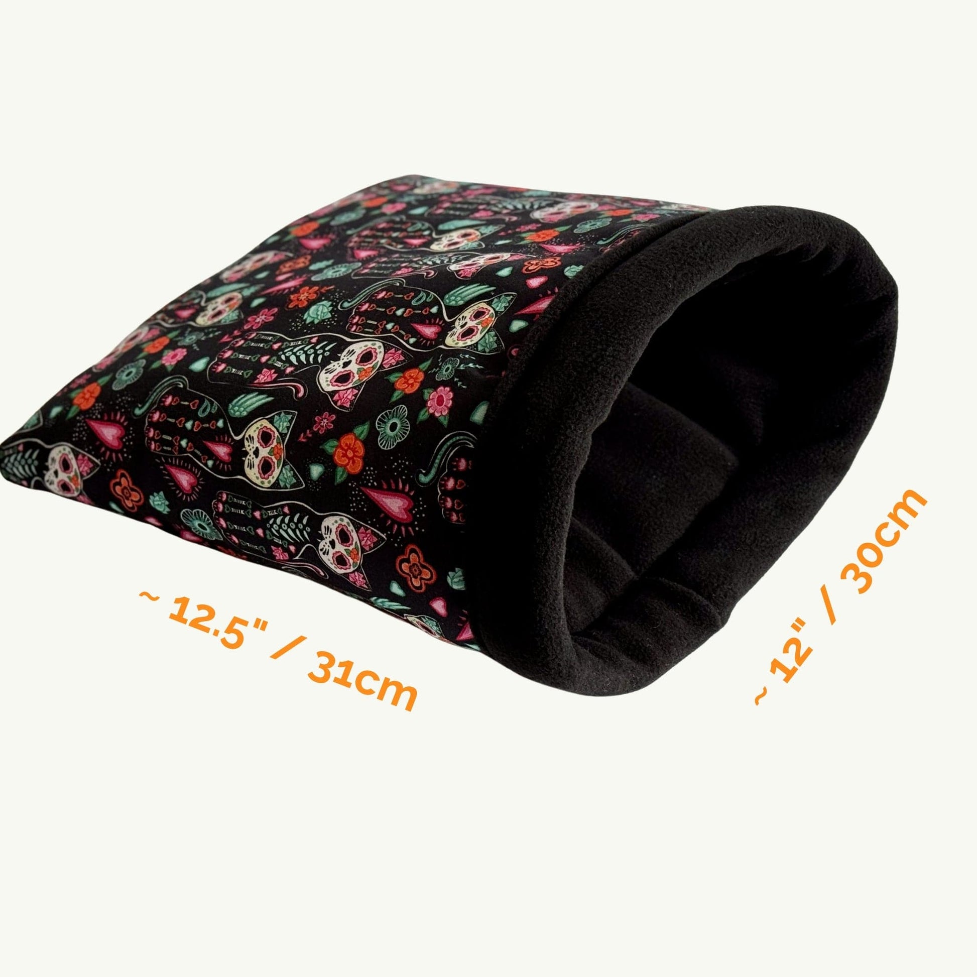 The Curious Catrina Snuggle Sack is a bewitchingly cozy tunnel, cloaked in midnight-black fabric adorned with vibrant sugar skulls and petals in haunted hues—think pinks, purples, teals, and sunny gold. Lined with plush fleece for the ultimate gothic-glam embrace, this 12-by-12.5-inch hideaway is perfectly sized for guinea pigs or other small familiars seeking a charming crypt of comfort. Displayed against a simple background for maximum spook-chic effect.