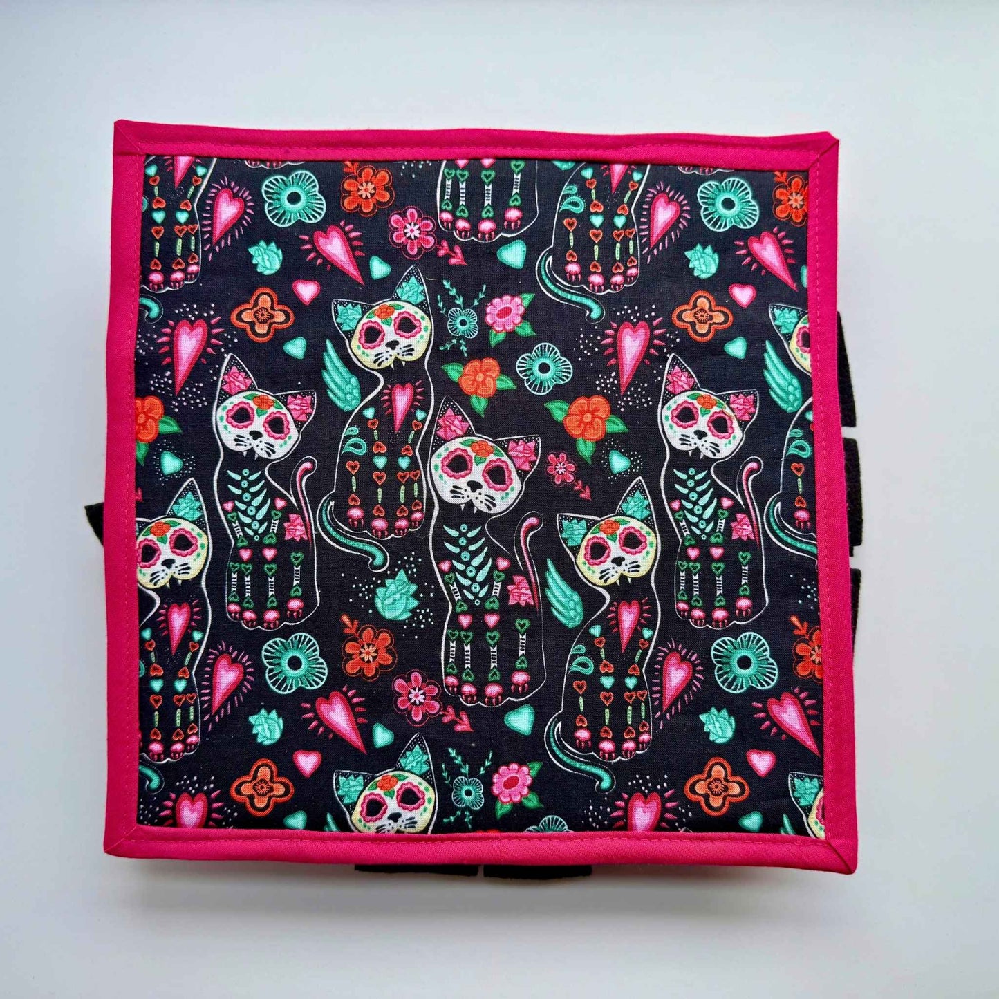 A gothic-glam snuffle mat: black cats with sugar-skull faces, florals, and hearts on pink trim—spooky-cute treat hunt for guinea pigs!.