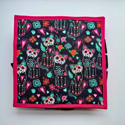 A gothic-glam snuffle mat: black cats with sugar-skull faces, florals, and hearts on pink trim—spooky-cute treat hunt for guinea pigs!.