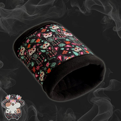 The Curious Catrina Fleece Tunnel enchants with gothic-glam flair—a plush black tunnel for guinea pigs, adorned in lively sugar skull cats and whimsical blossoms swirling across a dusky, smoky backdrop. A tiny illustrated mouse peeks playfully from the bottom left corner, adding a dash of adorable mischief for your spooky-cute companion.
