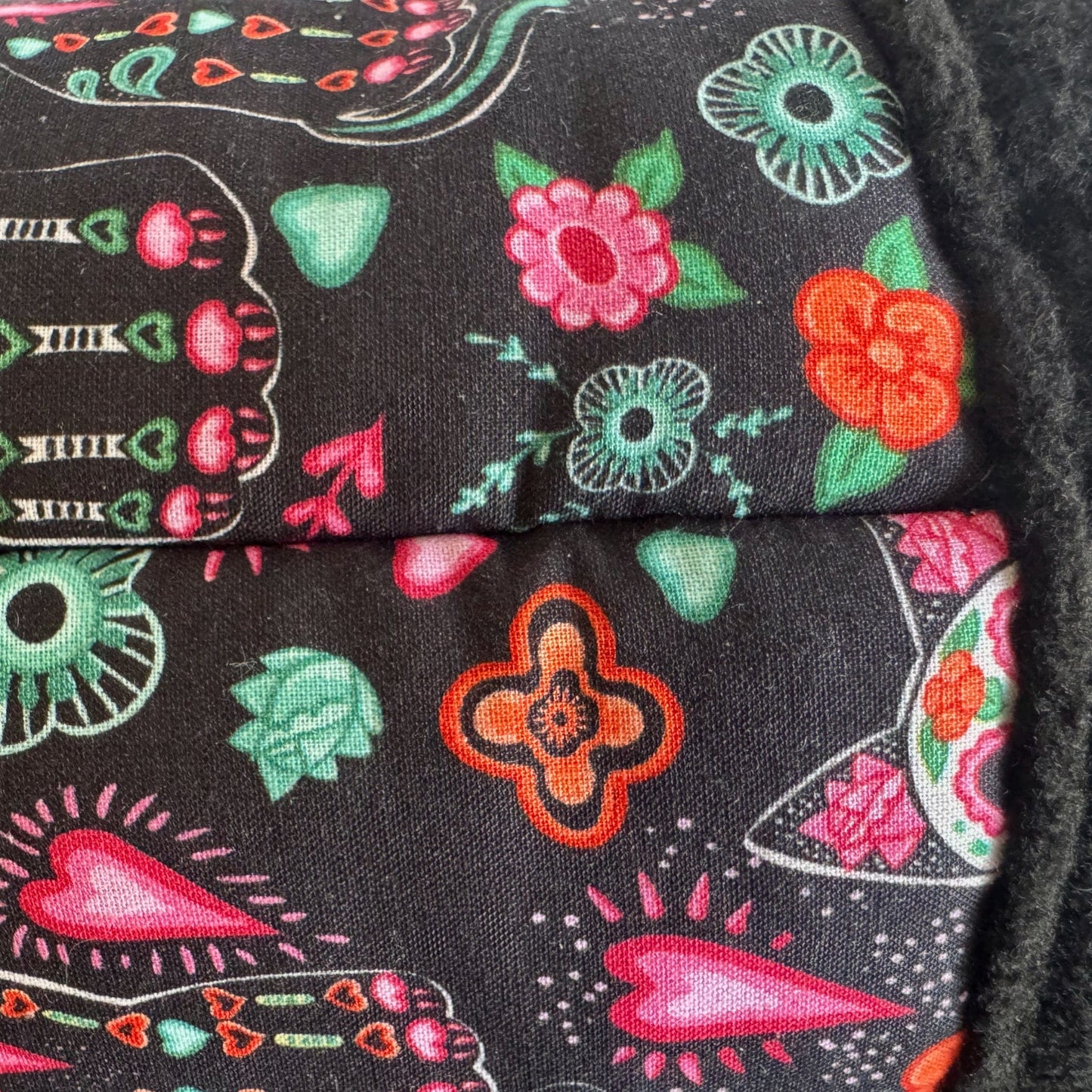 Enchanting close-up of midnight-black fleece, lavishly adorned with vivid pink and crimson blossoms, emerald leaves, and whimsical orange hearts. Neatly stitched seams add a touch of gothic glamour—perfect for the Curious Catrina Fleece Tunnel, inviting small pets to burrow in spooky-cute style.