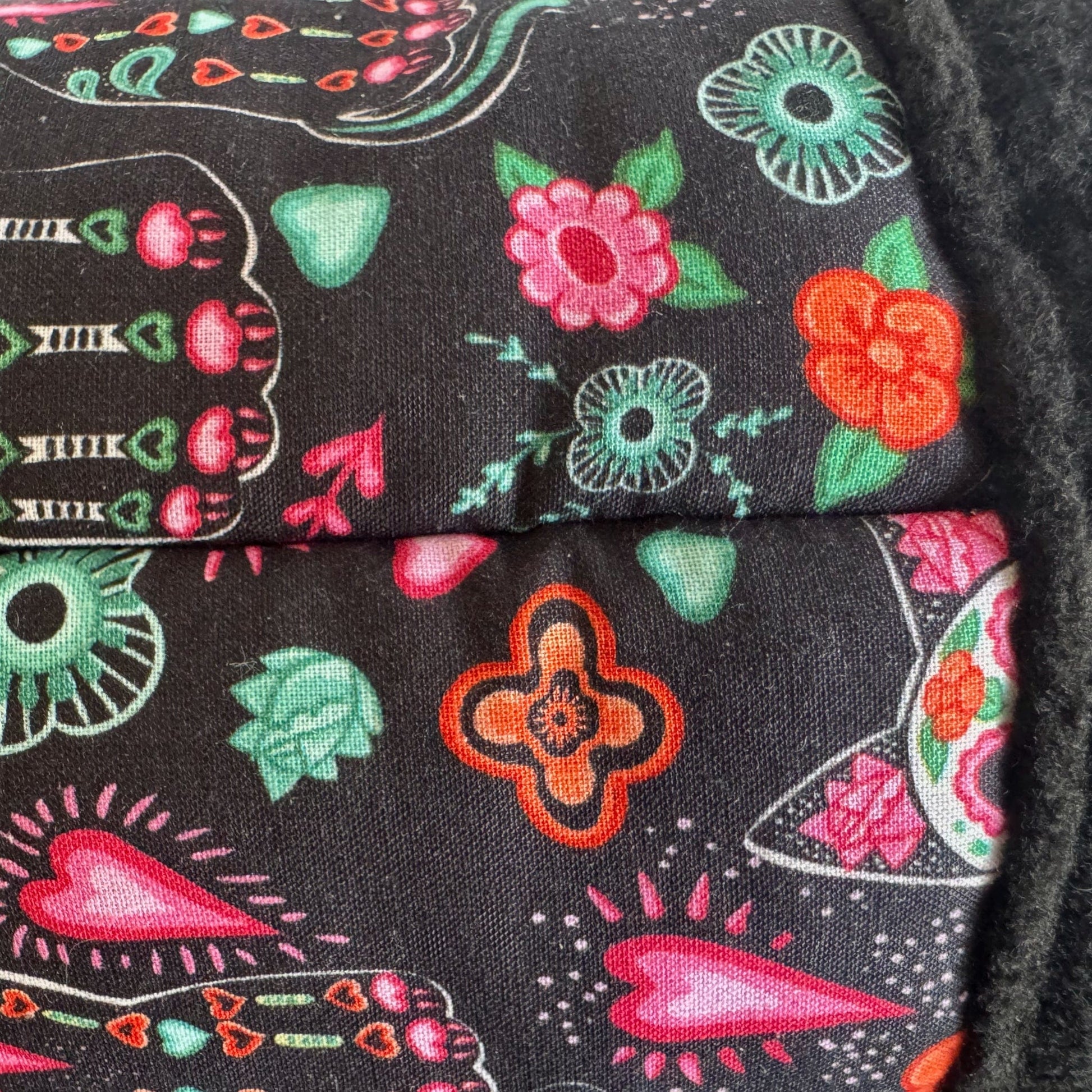 Enchanting close-up of midnight-black fleece, lavishly adorned with vivid pink and crimson blossoms, emerald leaves, and whimsical orange hearts. Neatly stitched seams add a touch of gothic glamour—perfect for the Curious Catrina Fleece Tunnel, inviting small pets to burrow in spooky-cute style.