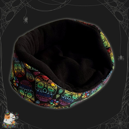 The Frightful Fiesta Fleece Bed radiates gothic-glam charm, enveloping little paws in midnight-black coziness. Its plush exterior dazzles with vibrant sugar skulls—smiling and sparkling—nestled against an enchanting shadowy backdrop swirling with silvery spiderwebs, mischievous spiders, and a whimsical black cat illustration with beguiling eyes. A bewitchingly cute snuggle spot from the Frightful Fiesta collection, perfect for pampered guinea pigs or tiny pet ghouls seeking comfort in spooky style.