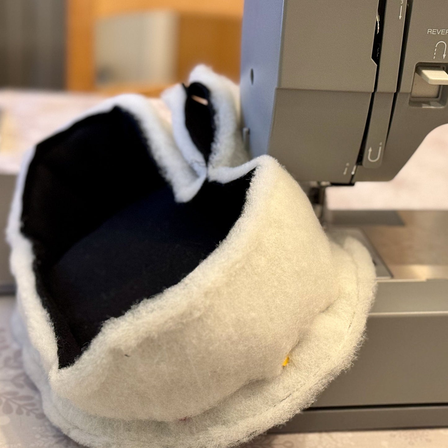 A sewing machine whirs away, conjuring a hauntingly adorable Frightful Fiesta Fleece Bed from swirling black and white fabric. Ghostly-soft fleece and patterned scraps tumble over the machine, ready to cradle your guinea pig in gothic-glam coziness.