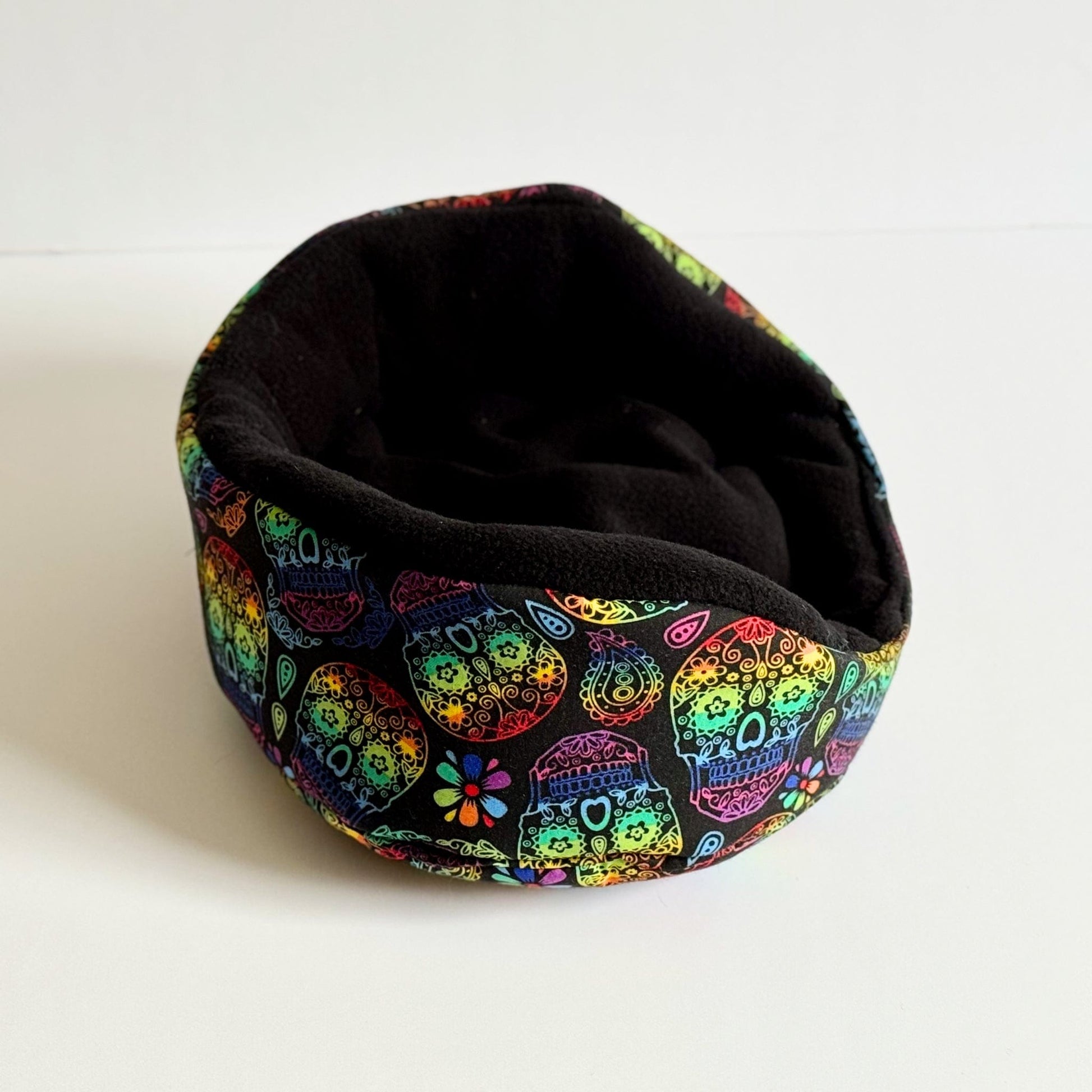 The Frightful Fiesta Fleece Bed is a plush, round haven for small pets, gleaming with gothic-glam allure. Its velvety black interior invites cozy naps, while the outer fabric shimmers with a parade of vibrant sugar skulls and enchanting florals—swirling purples, fiery reds, and pops of neon nestled on midnight black. This whimsically spooky bed adds a dash of haunted elegance to your guinea pigs lair or any small animal’s boudoir—perfect for creatures who dream among shadows and blooms alike.