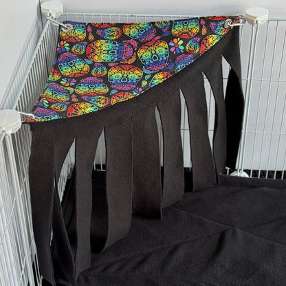 The Frightful Fiesta Corner Fleece Forest awaits your spooky-cute companion—inky black fleece strips dangle eerily, creating a mysterious fringe for midnight hide-and-seek, while a vibrant sugar skull hammock glimmers with haunting neon greens, pinks, and golds. A gothic-glam hideaway for guinea pigs or small pets to revel in cozy shadows and fiesta flair!.