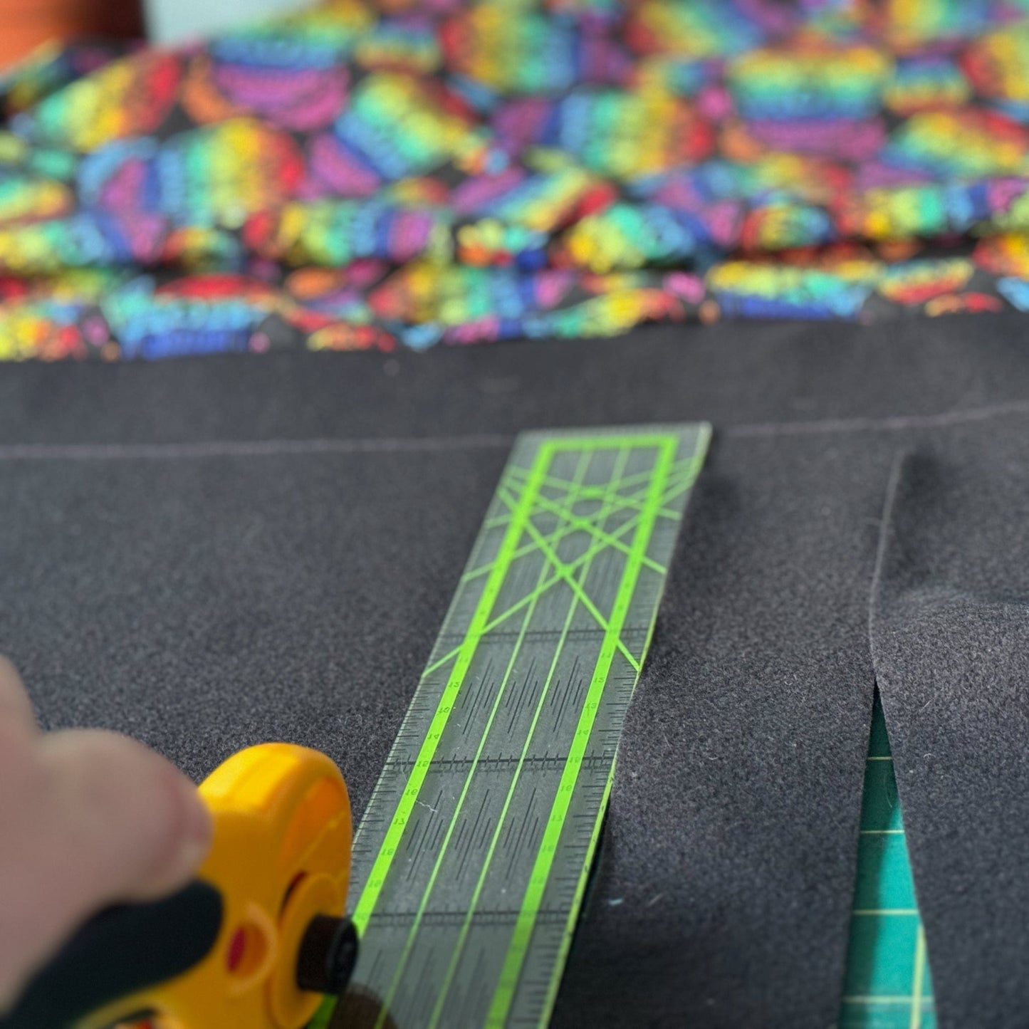 A close-up of elegant hands wielding a rotary cutter and ruler, delicately slicing through midnight-black fabric. In the background, a vibrant Frightful Fiesta Large 2x1 Fleece Forest bursts with gothic-glam colors—think jewel-toned purples and fiery oranges—casting an enchanting glow. The scene is spellbindingly perfect for crafting a cozy hideaway your guinea pigs (or other small familiars) will adore haunting!.
