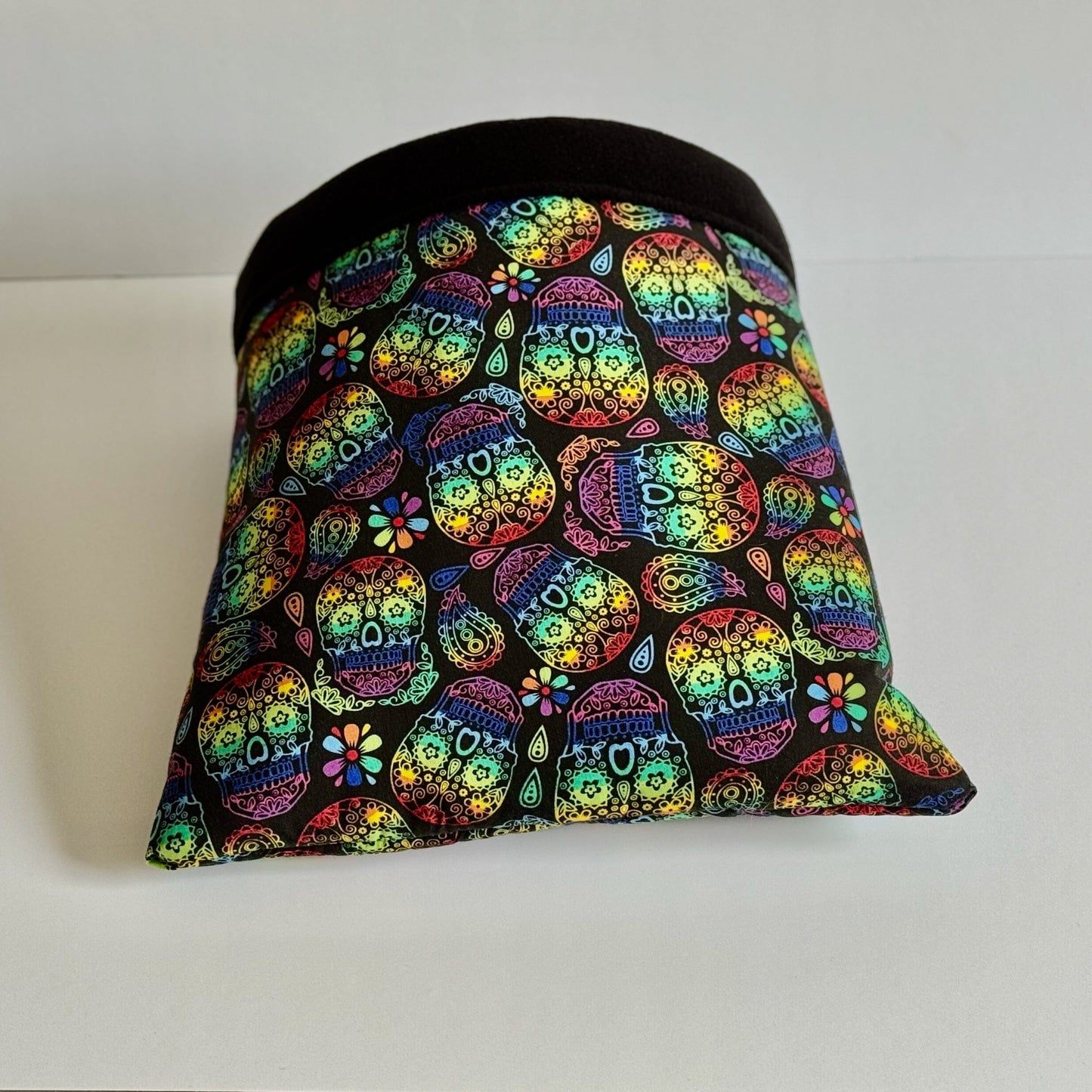 The Frightful Fiesta Snuggle Sack—a bewitching pet hideaway—enchants with dazzling sugar skulls and gothic blooms swirling across midnight-black fleece. A sleek, jet-black band frames the entrance, inviting your small companion to burrow into plush comfort. Shown in all its spooky-chic glory against a crisp white backdrop.