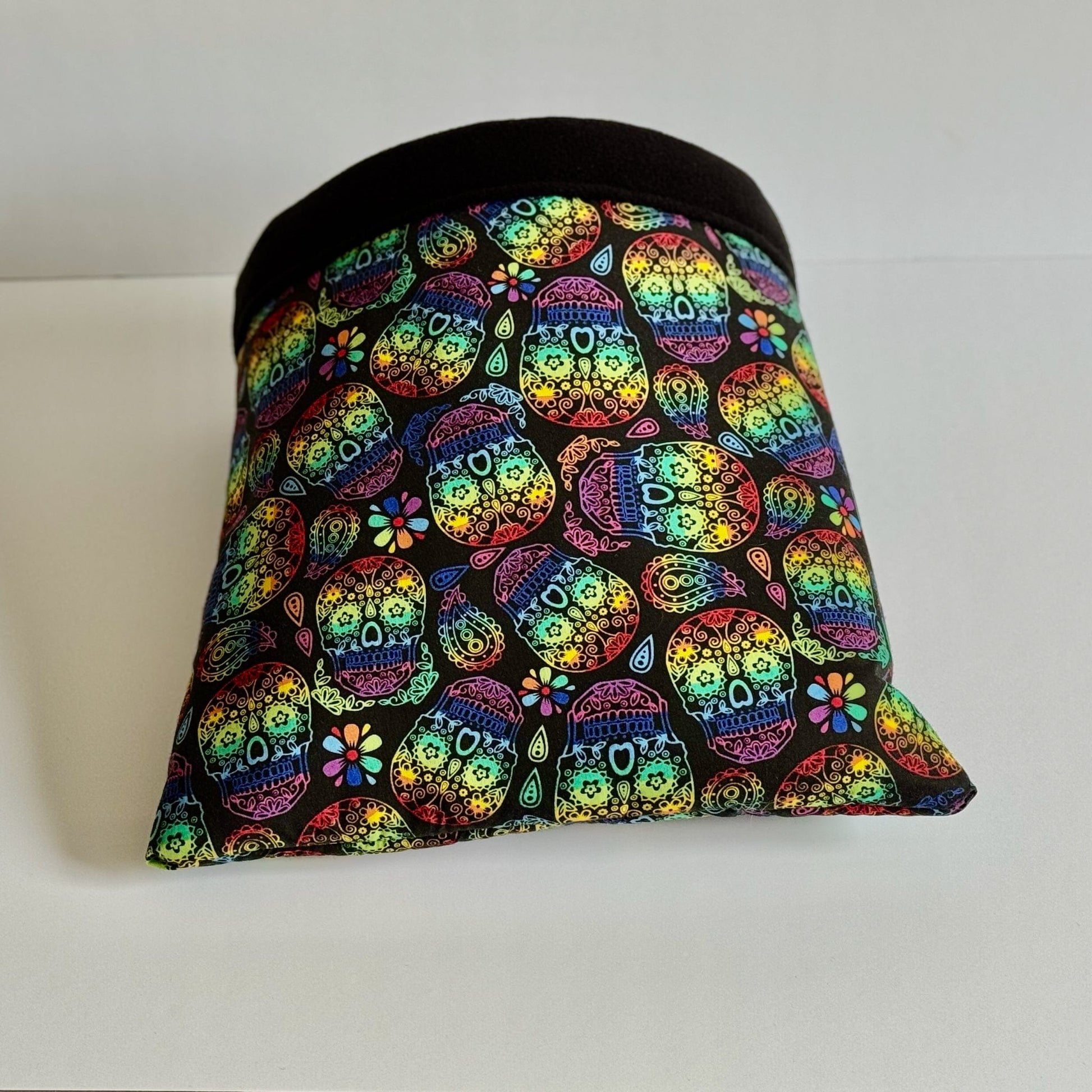 The Frightful Fiesta Snuggle Sack—a bewitching pet hideaway—enchants with dazzling sugar skulls and gothic blooms swirling across midnight-black fleece. A sleek, jet-black band frames the entrance, inviting your small companion to burrow into plush comfort. Shown in all its spooky-chic glory against a crisp white backdrop.