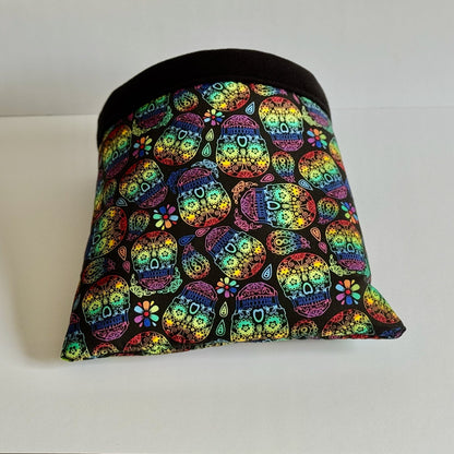 The Frightful Fiesta Snuggle Sack—a bewitching pet hideaway—enchants with dazzling sugar skulls and gothic blooms swirling across midnight-black fleece. A sleek, jet-black band frames the entrance, inviting your small companion to burrow into plush comfort. Shown in all its spooky-chic glory against a crisp white backdrop.