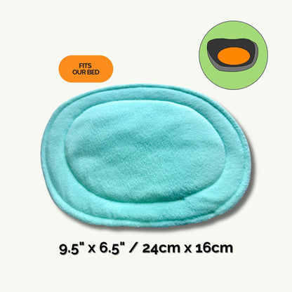 A whimsically gothic light blue pee pad, shaped like a moonlit oval with softly rounded edges, measures 9.5 by 6.5 inches (24 by 16 cm)—the perfect haunt for your small companion’s cozy naps. Above the pad, a charming diagram conjures up its ideal match: our plush coffin-bed, so your little beastie can rest in style. An eye-catching pumpkin-orange label declares, “Fits Our Bed.” Text reads: “Pee Pads | Haunt messes away—make daily clean-up simply bewitching!”.
