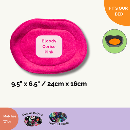 A bewitchingly bright oval pet bed cover in Bloody Cerise Pink (9.5 x 6.5 in / 24 x 16 cm) beckons your small furry familiars for sweet slumbers. Nestled beside it are matching pee pads from our Curious Catrina collection—think gothic florals and playful skulls—ready to keep every midnight romp tidy. Fit icons flutter like mischievous spirits nearby, all elegantly displayed on a pale backdrop to let the vivid pink pop with enchanting flair.