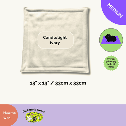 A plush ivory fleece pee pad (13x13in) haunts softly—perfect for guinea pigs. Set on a pale, dreamy Trickster’s Treats backdrop.