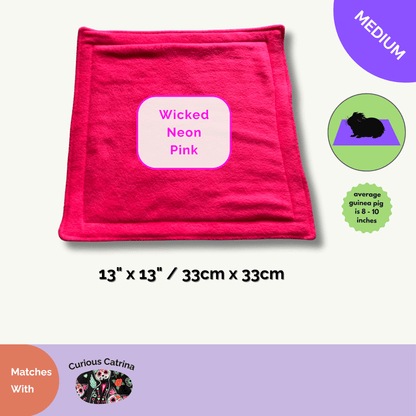 A bewitching Wicked Neon Pink fleece mat (13x13in/33x33cm) glows with gothic glamour, perfect for your guinea pig’s midnight soirees. Matching Curious Catrina Pee Pads—adorned with charming sugar skulls—promise easy cleanup and fanciful fun. The scene is sprinkled with spook-tacular accessory ideas, inspiring a hauntingly cute home for your small companion.