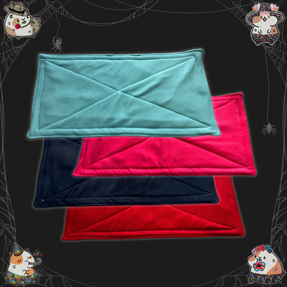 Four snuggly fleece liners and matching pee pads—one each in enchanting teal, bubblegum pink, midnight black, and blood-red—are neatly stacked atop a moody dark backdrop. Cute gothic cartoon critters gaze curiously from the shadows, while playful spider webs and friendly little spiders adorn the corners, spinning cozy magic for your beloved small pets.