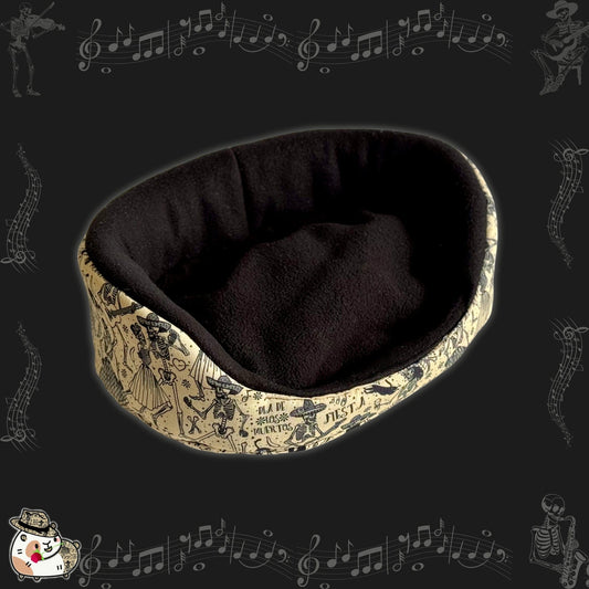 Spooky-cute alt text: The Tombstone Tango Fleece Bed is an enchanting oval cuddle spot for guinea pigs, crafted with a plush black fleece interior and a creamy pale outer layer. Bewitching black musical notes and charming skeletons waltz across the cream fabric, conjuring gothic-glam vibes from our Tombstone Tango collection. Perfect for tiny familiars who love to lounge in ghostly comfort!.
