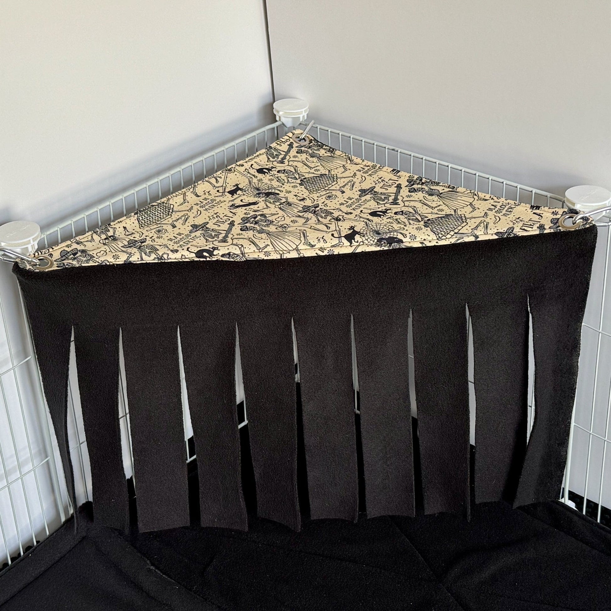 The Tombstone Tango Corner Fleece Forest is a whimsically spooky hammock for small pets, featuring a patterned top adorned with gothic tombstones and moonlit motifs. Wispy black fleece fringe drapes below, creating an enchanting curtain of shadows. Designed to nestle into the corner of your pets cage, this eerie-cute forest attaches easily to white wire panels—providing guinea pigs and other tiny familiars with a plush hideaway for midnight mischief and daytime dreams.