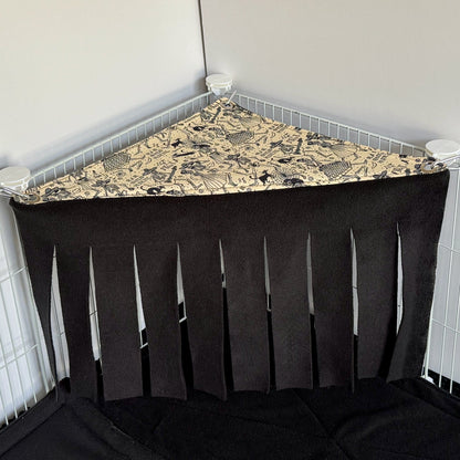 The Tombstone Tango Corner Fleece Forest is a whimsically spooky hammock for small pets, featuring a patterned top adorned with gothic tombstones and moonlit motifs. Wispy black fleece fringe drapes below, creating an enchanting curtain of shadows. Designed to nestle into the corner of your pets cage, this eerie-cute forest attaches easily to white wire panels—providing guinea pigs and other tiny familiars with a plush hideaway for midnight mischief and daytime dreams.