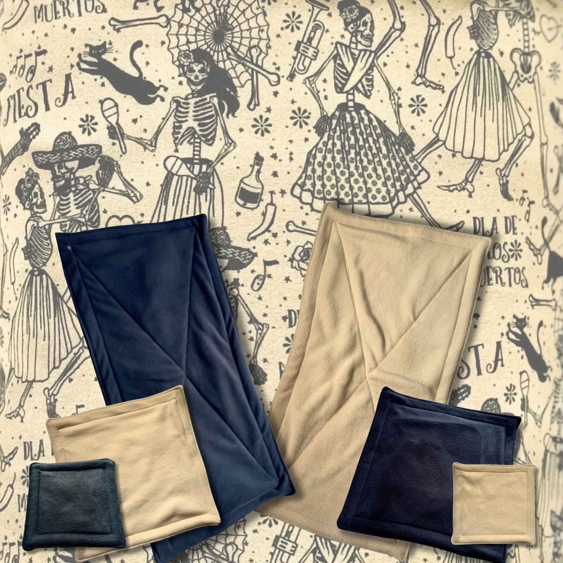 Beige and navy Tombstone Tango Pee Pads, folded atop Día de Muertos fabric with waltzing skeletons—spooky-chic comfort for pets.