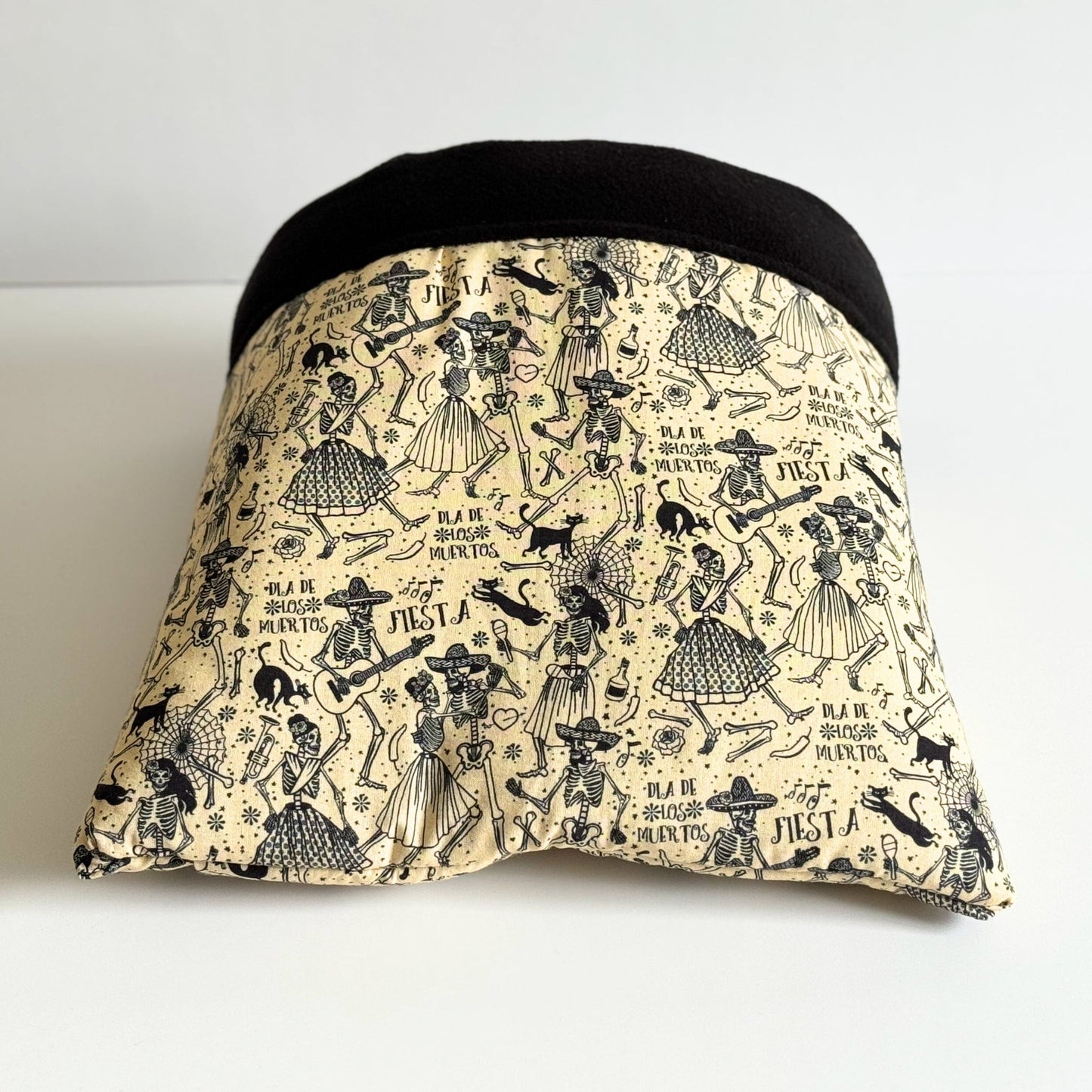 The Tombstone Tango Snuggle Sack is a plush fleece sleep sack for guinea pigs and small pets, featuring a dramatic black top and a soft beige base. Festive skeletons in swirling party attire dance across the fabric, framed by gothic florals and playful Día de Muertos script. This spooky-cute cocoon is designed to enchant your pet’s dreams while keeping them warm and cuddled in gothic-glam comfort.