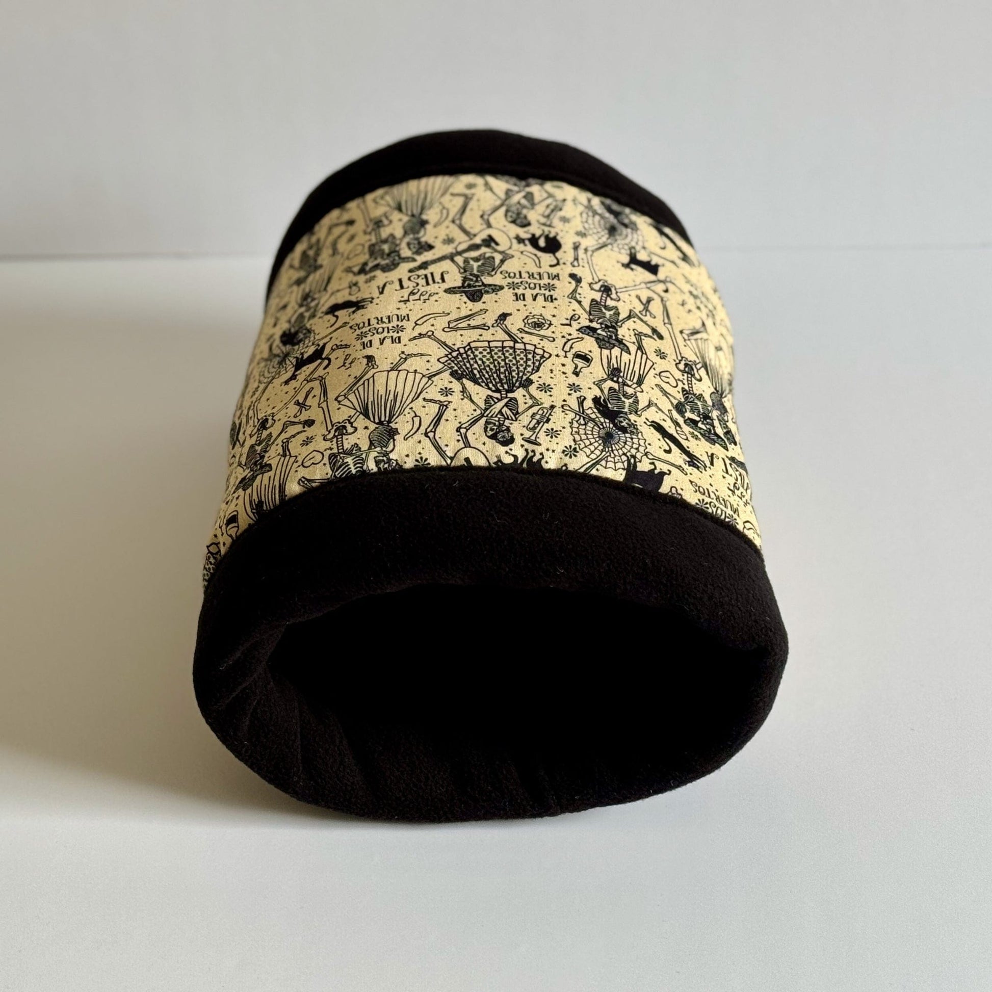 The Tombstone Tango Fleece Tunnel—a bewitching little haven for your spooky-cute companion—rests upon a ghostly white backdrop. This enchanting small pet tunnel is stitched from plush black fleece and hauntingly pale cream, bedecked with a gothic floral pattern featuring charming skeletons entwined in delicate blooms. Ideal as a cozy crypt for guinea pigs or other small creatures seeking stylish sanctuary.