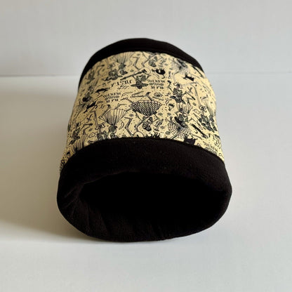 The Tombstone Tango Fleece Tunnel—a bewitching little haven for your spooky-cute companion—rests upon a ghostly white backdrop. This enchanting small pet tunnel is stitched from plush black fleece and hauntingly pale cream, bedecked with a gothic floral pattern featuring charming skeletons entwined in delicate blooms. Ideal as a cozy crypt for guinea pigs or other small creatures seeking stylish sanctuary.