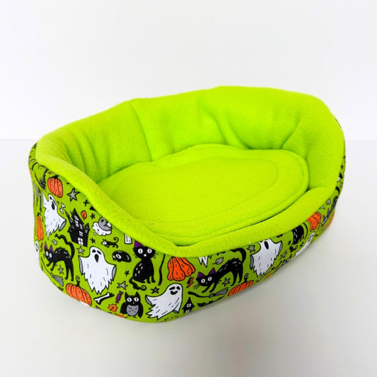 The Trickster's Treats Fleece Bed shimmers in bright green, with gothic ghosts, black cats, pumpkins, and bats haunting its cozy sides.