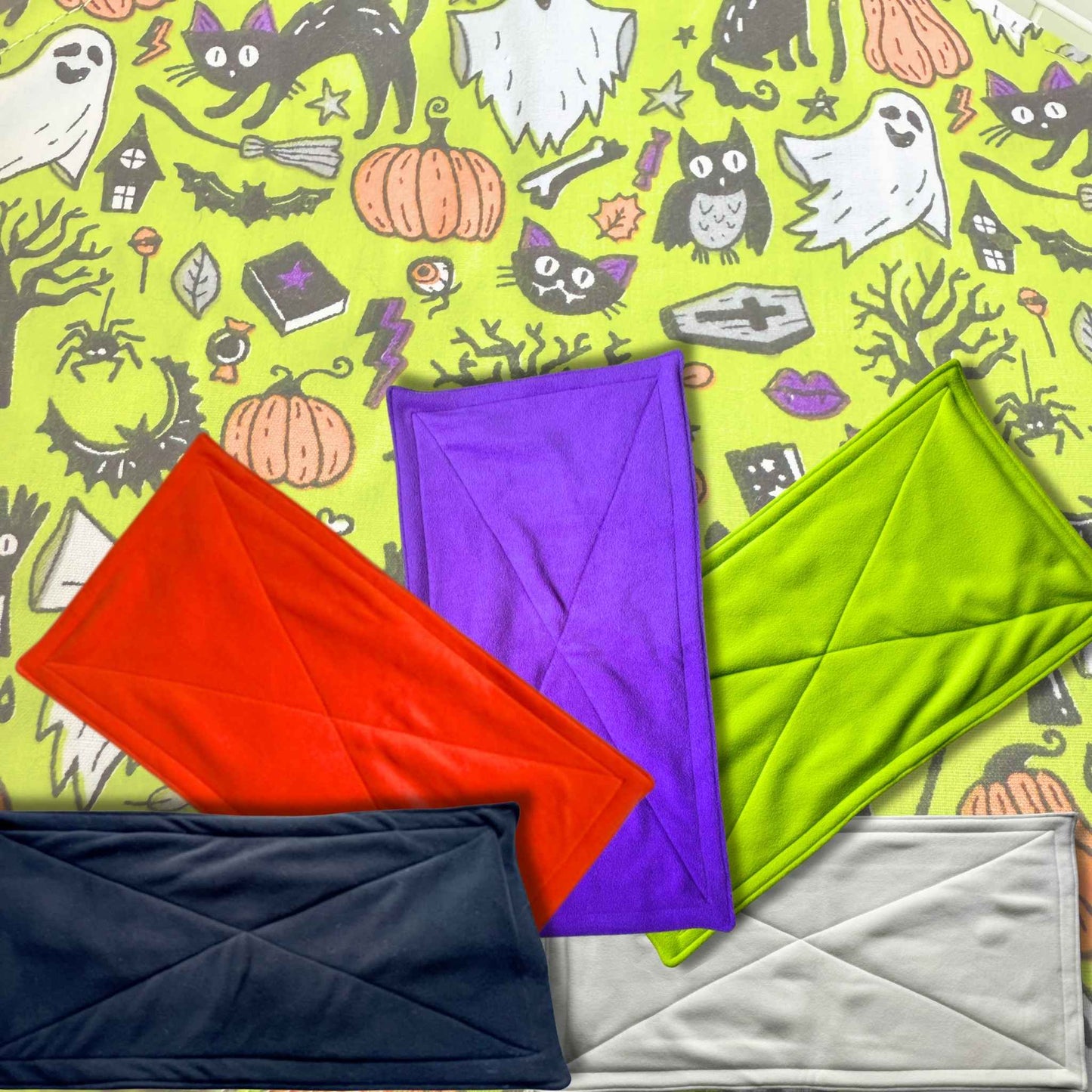 Enchant your cage with five goth-glam fleece pee pads—red, purple, green, black, white—resting on a spooky-cute Halloween haunt.